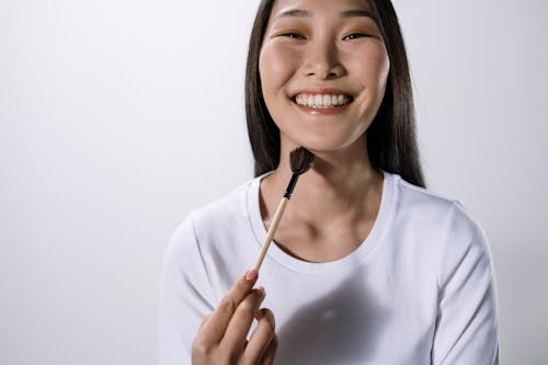 Woman in White Shirt Holding Brown and White Makeup Brush