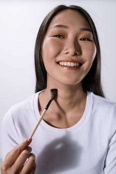 A cheerful woman with a makeup brush in a studio setting against a white background.