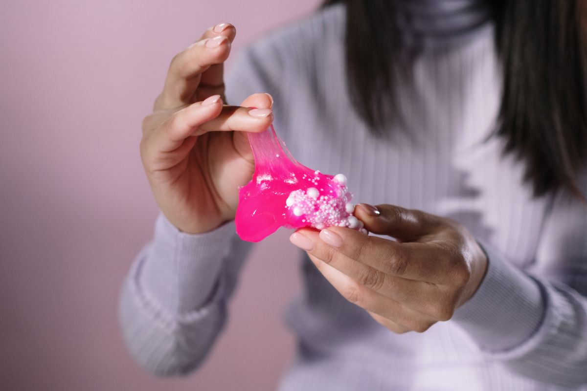 Hands stretching bright pink slime with white foam beads