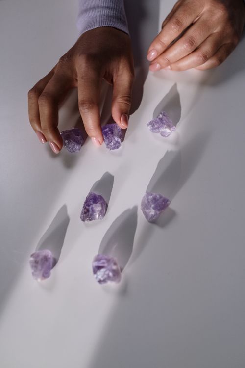 Free Close-up view of a hand arranging amethyst gemstones on a white surface, highlighting their natural beauty. Stock Photo