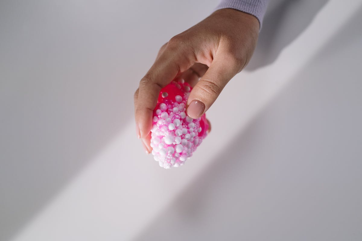 Primo piano di mani che tengono slime rosa con perline di schiuma