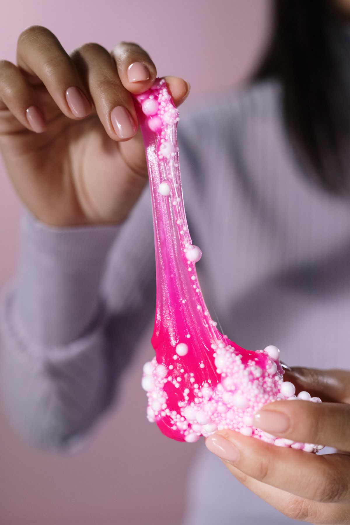 Hands stretching bright pink slime with foam beads