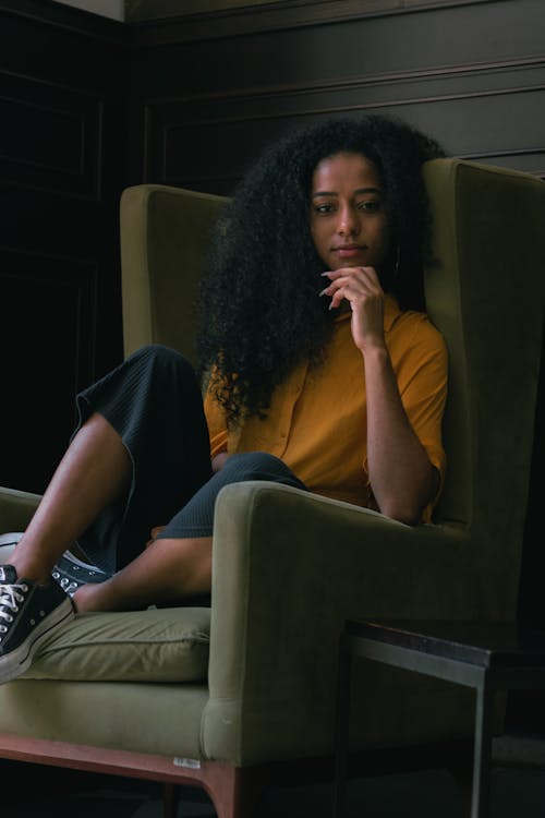 Thoughtful young black woman sitting in green armchair