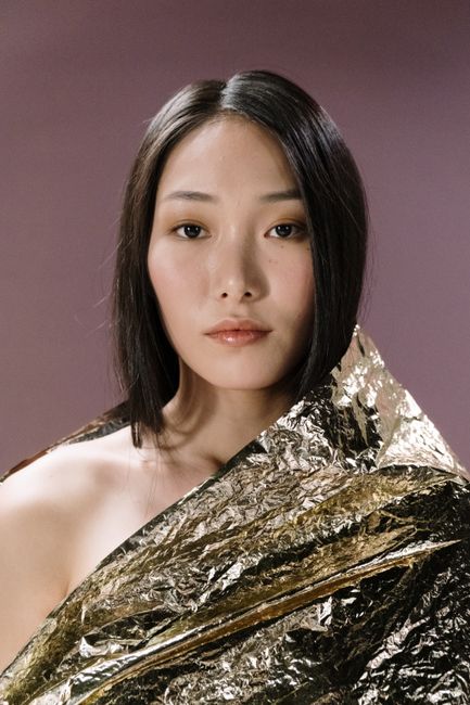 Studio portrait of a woman wrapped in gold foil, exuding elegance and softness.