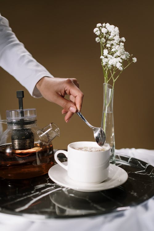 A person Holding a Stainless Spoon Over the White Cup