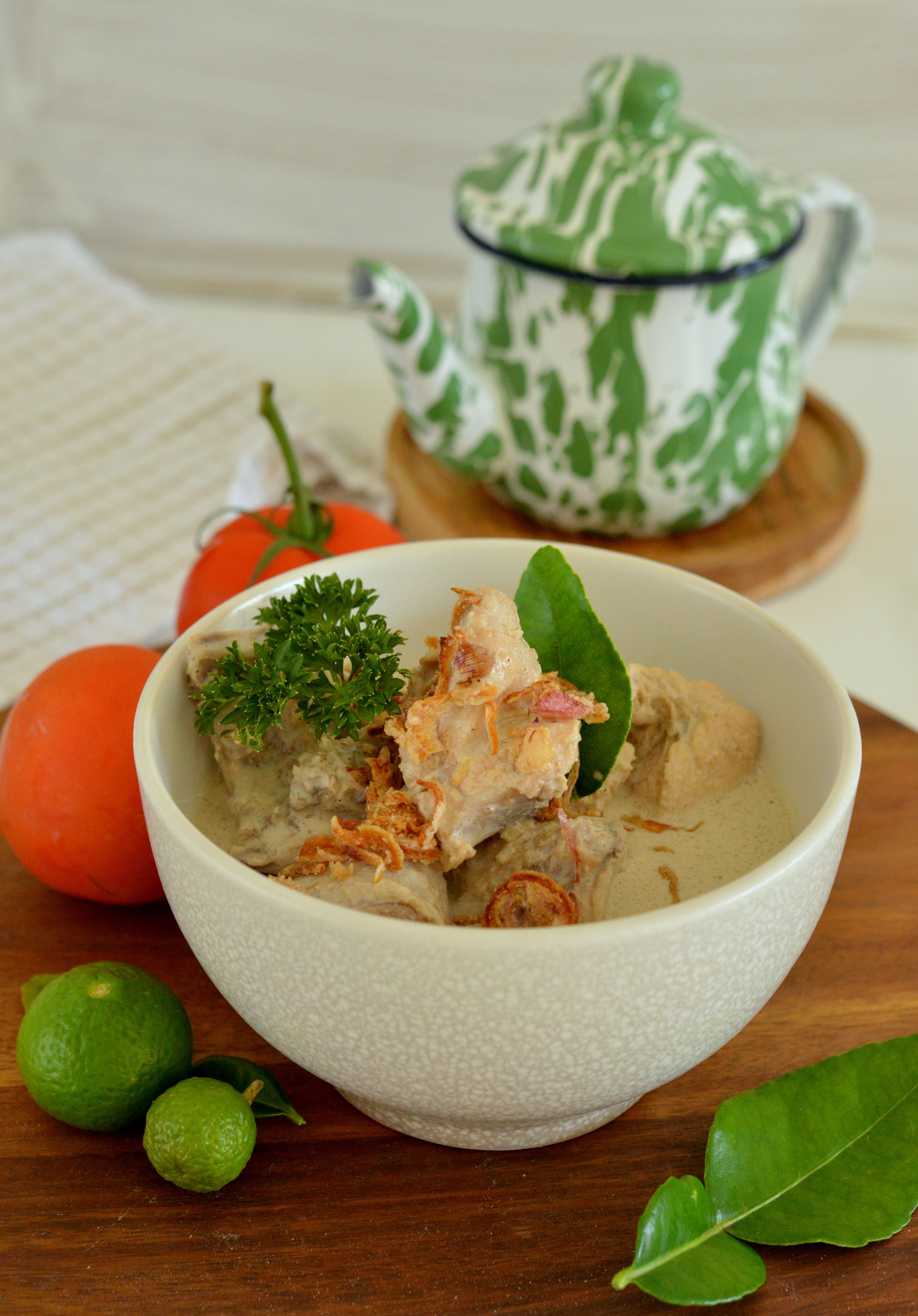 Delicious bowl of traditional Asian dish with fresh herbs and citrus beside a patterned teapot.