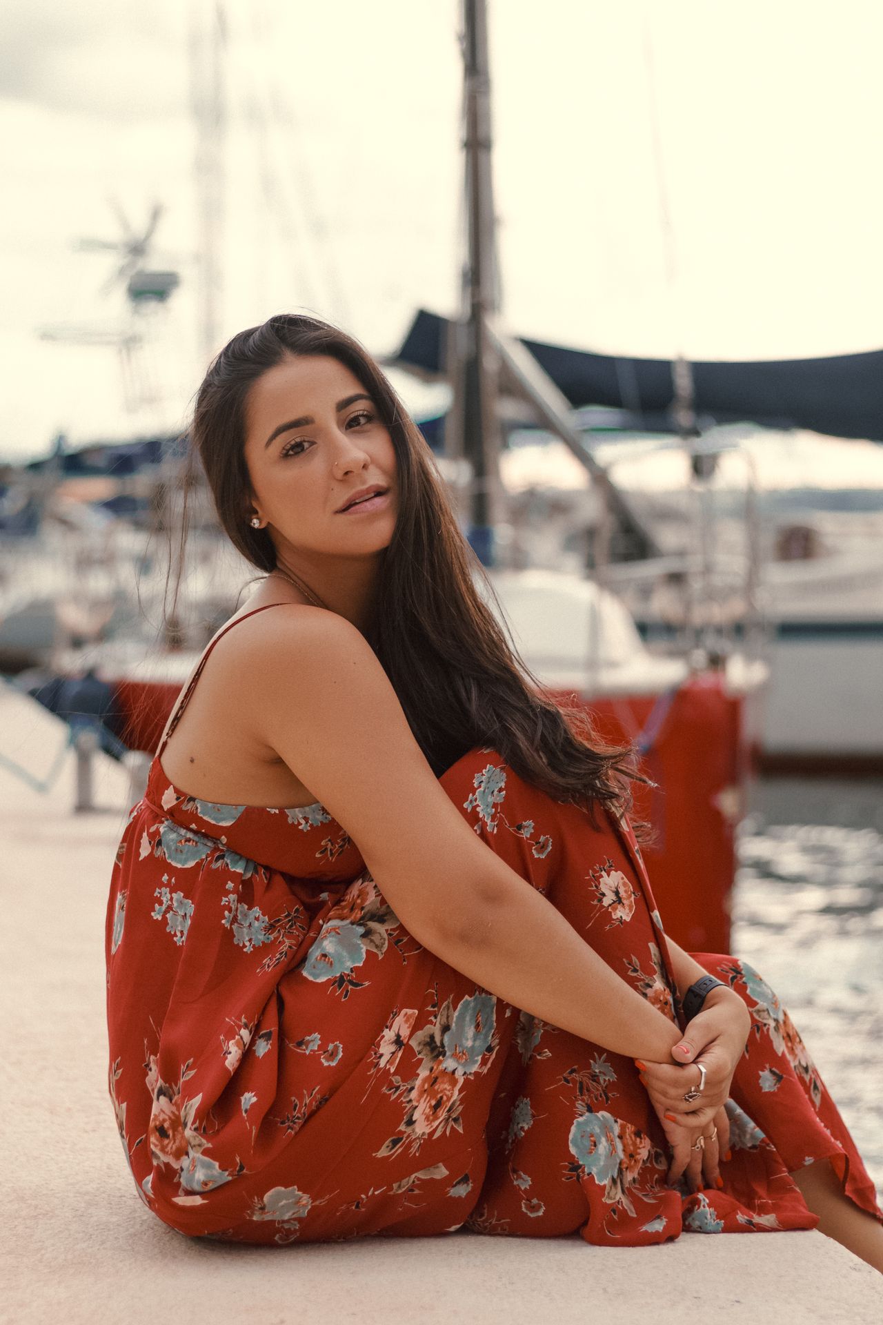 Woman in a red floral maxi dress sitting by a marina, a pretty daytime red dress outfit