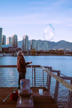A man standing on a dock in Vancouver creates a giant soap bubble against a skyline.