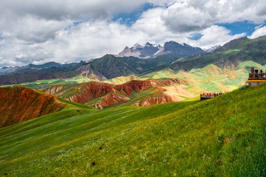 A vibrant mountain landscape with green hills and a scenic viewing deck under white clouds.