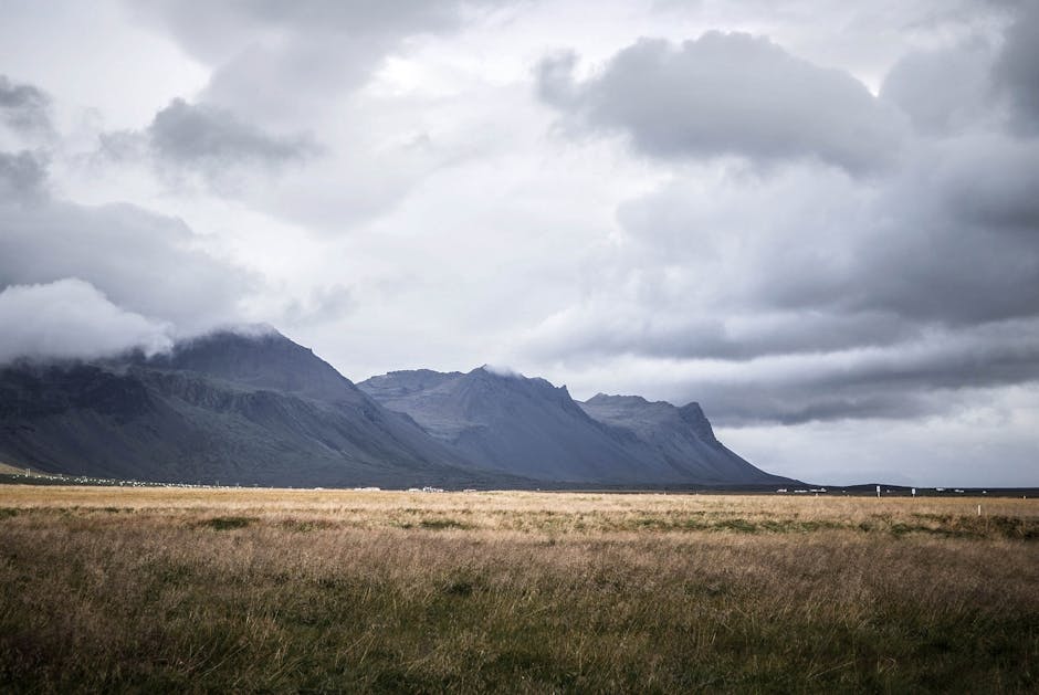 Scenic view of mountains under a cloudy sky with vast grassy fields in the foreground.
