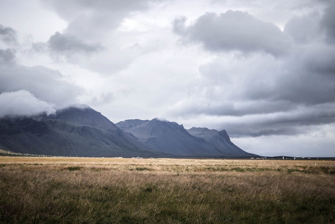 Brown Grass Field and Gray Mountains Under Gray Clouds