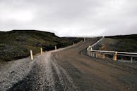 在乌云密布的天空下，一条蜿蜒的砾石路穿过崎岖的乡村，缓缓向上坡延伸