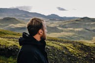 一名身穿黑色夹克的男子在白天欣赏广阔的山地景观，捕捉到了户外冒险的本质