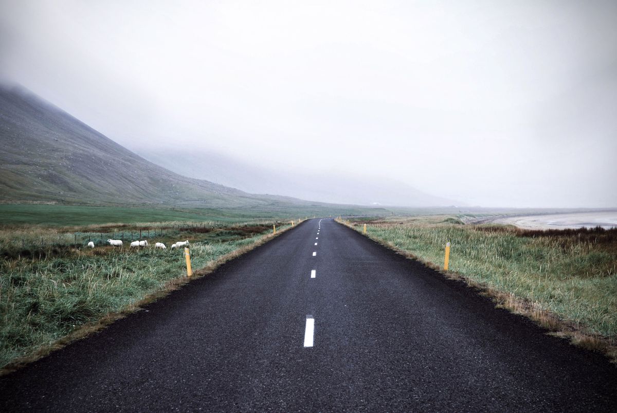 A paved road through the green landscape of Iceland with mountains in the distance