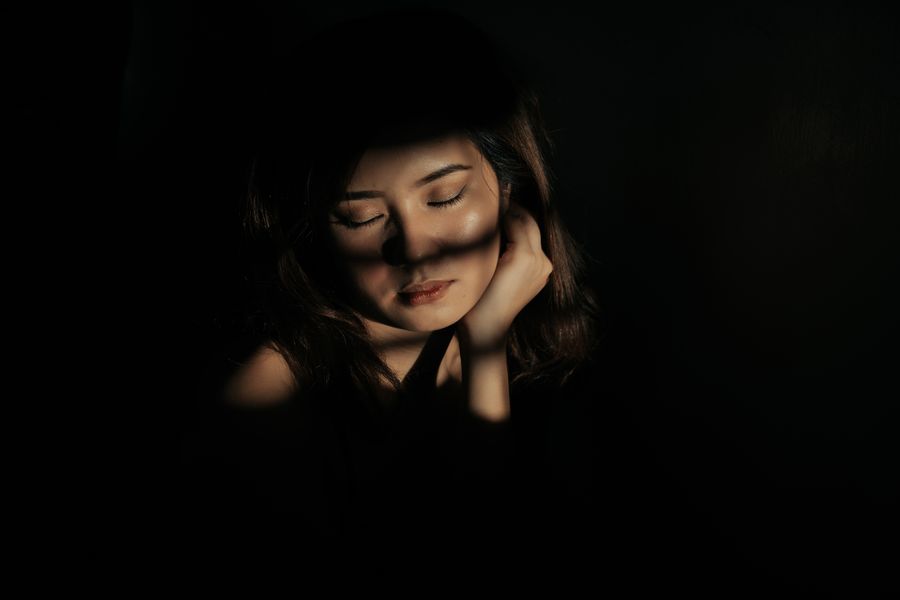 A woman in shadow, hands to her face, in soft light