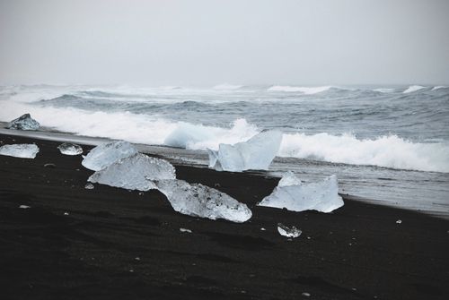 Free Icebergs on a black sand beach with ocean waves, creating a dramatic winter seascape. Stock Photo
