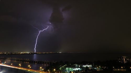Free A powerful lightning bolt illuminates the night sky over a city with a distant skyline. Stock Photo