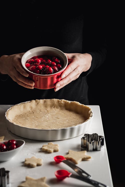 A Person Holding a Bowl of Cherries Over the Pie Crust