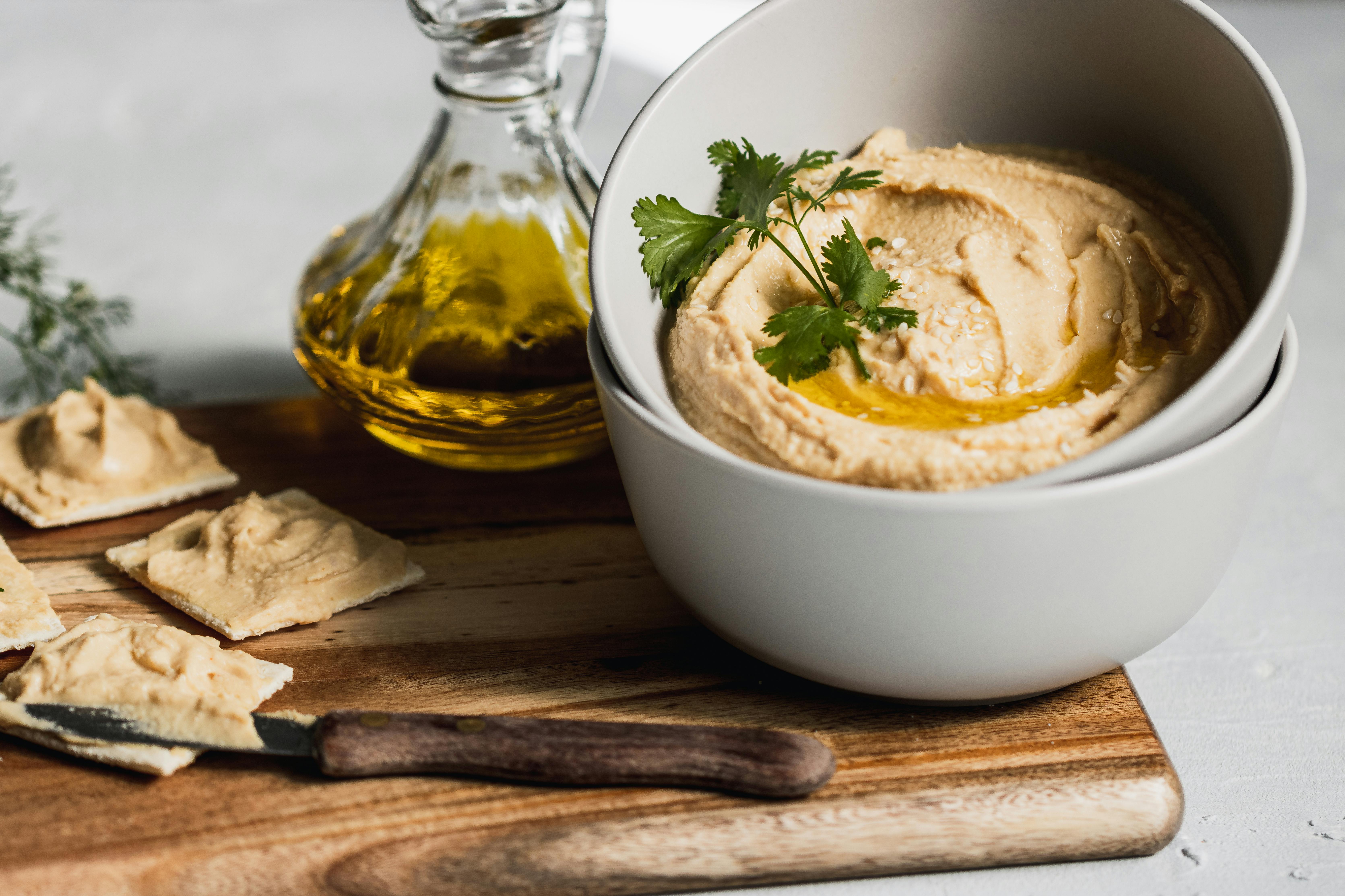 Free Close-up of a bowl of creamy hummus topped with olive oil and herbs, accompanied by crackers. Stock Photo