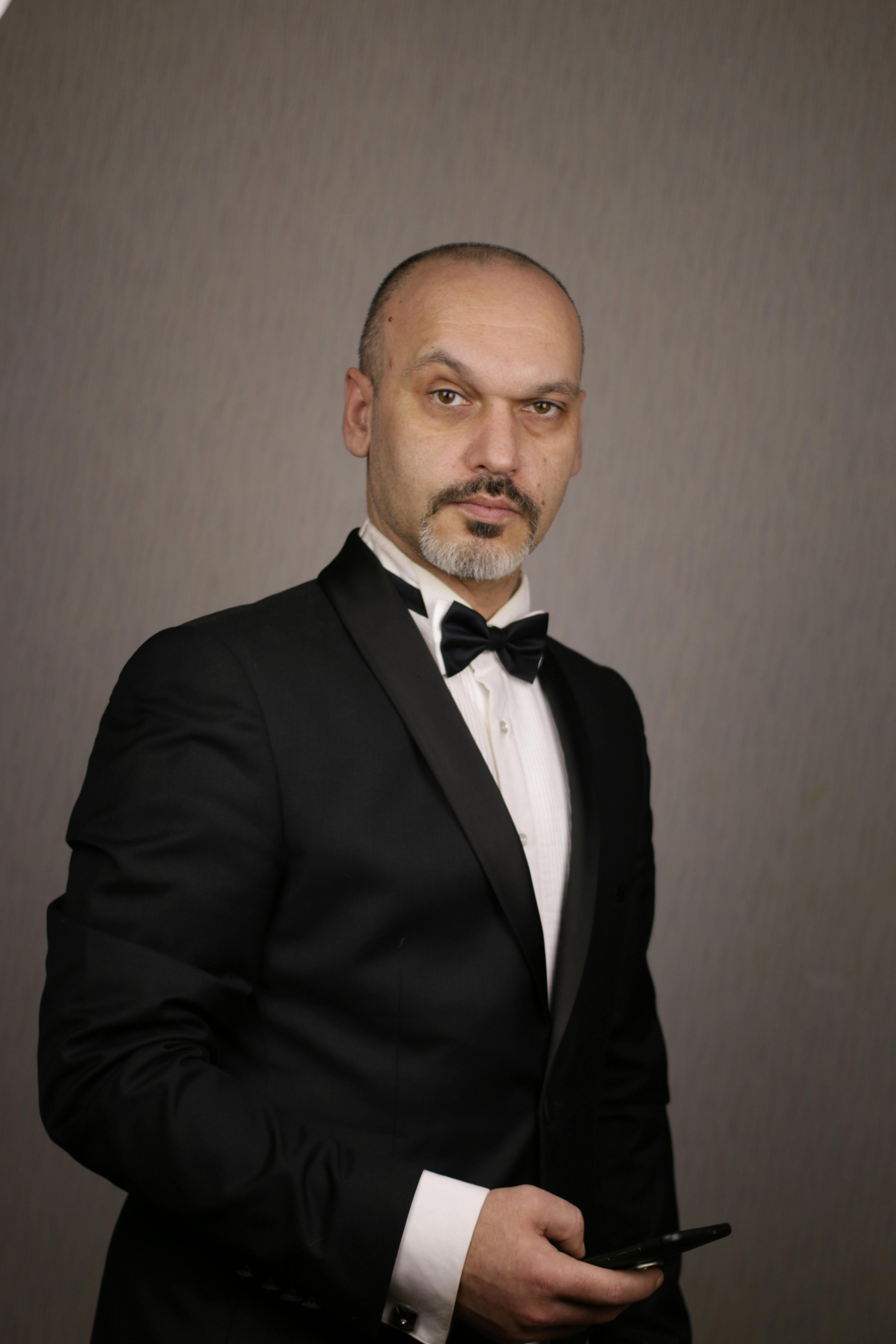 Portrait of a bald man in a black suit holding a smartphone, showcasing elegance in a studio setting.
