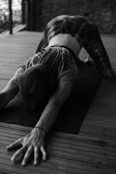 Black and white photo of a woman stretching on a yoga mat in a serene studio setting.