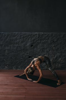Female practicing yoga pose indoors on mat in dim lighting for fitness.