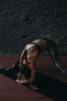 A woman in activewear doing a yoga stretch on a mat indoors, promoting fitness and healthy lifestyle.