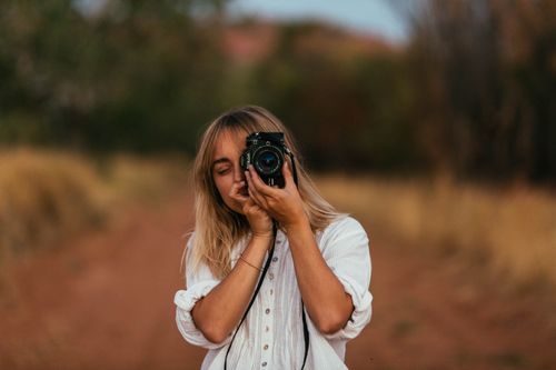 Free A blonde woman in a white top taking a photo with a camera outdoors on a nature trail. Stock Photo
