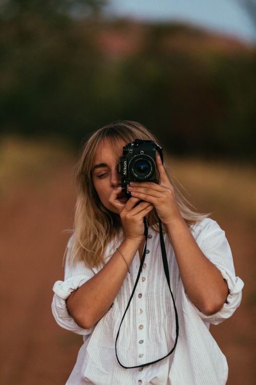Free A young woman in white takes a nature photo with a DSLR camera outdoors. Stock Photo