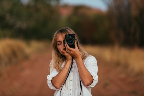 Free Female photographer in white shirt taking photos in natural outdoor setting. Stock Photo