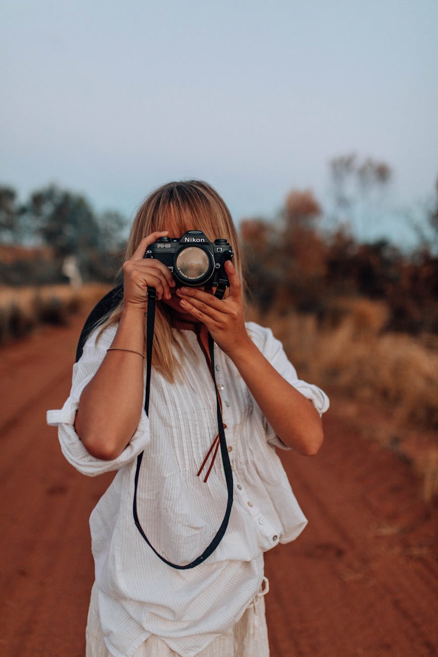 Woman capturing a scenic view with a DSLR camera on a dirt road in the countryside.