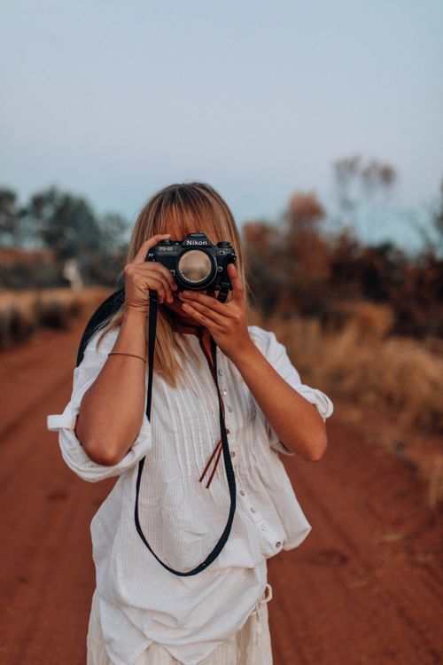 Free Woman capturing a scenic view with a DSLR camera on a dirt road in the countryside. Stock Photo