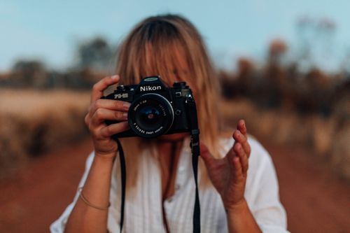 Free Woman holding a Nikon camera in an outdoor natural setting. Capturing the beauty of nature. Stock Photo