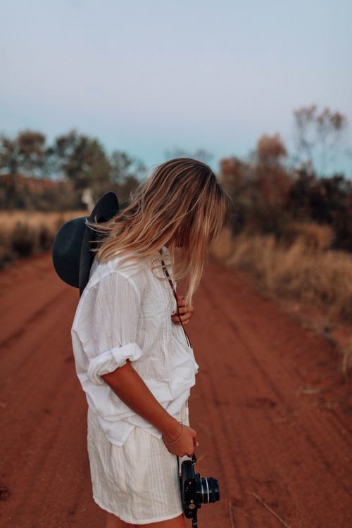 Free Woman in white dress with camera and hat on unpaved road during summer trip. Stock Photo