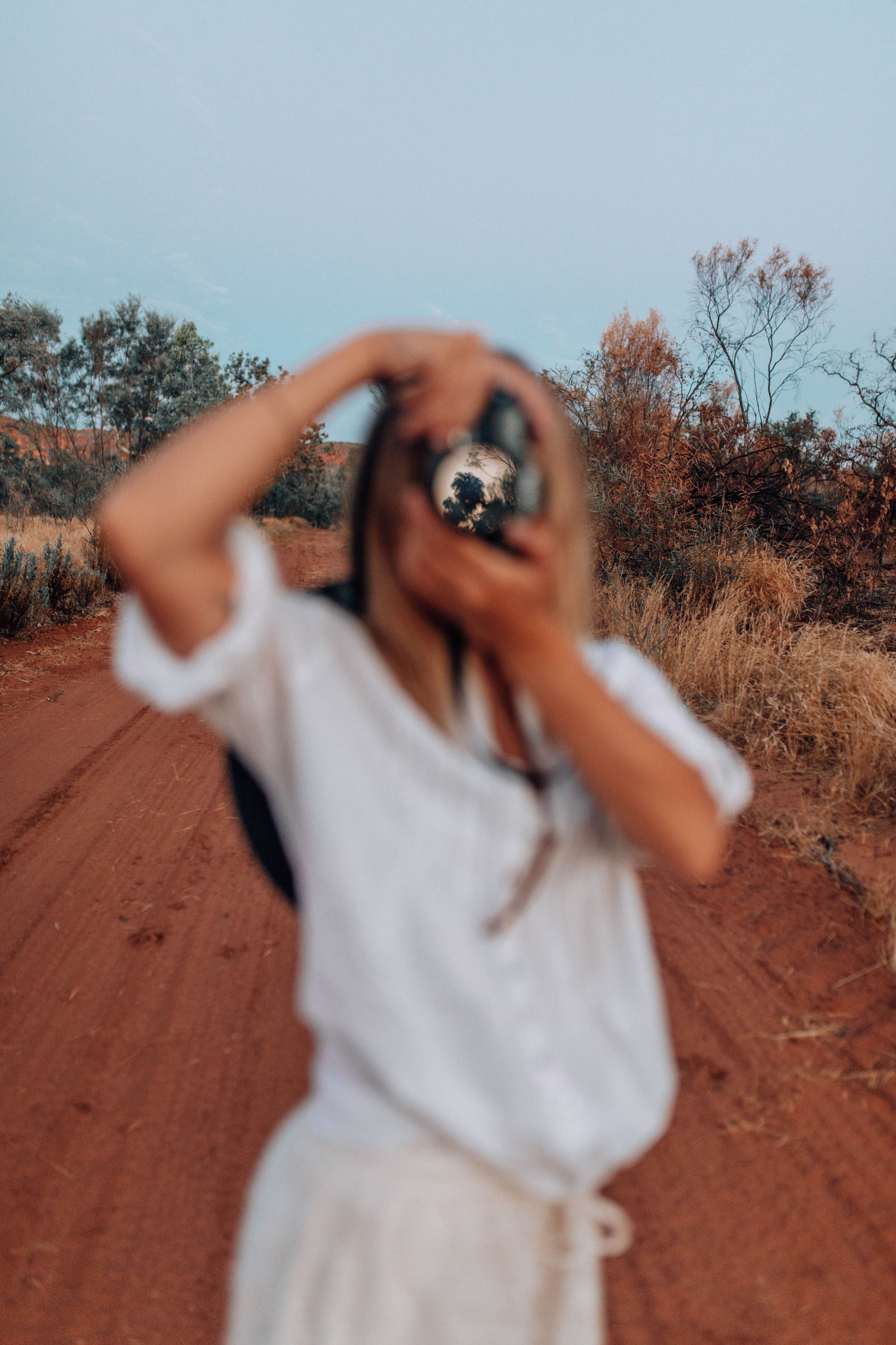 Blurred woman photographing a rural scene on a red dirt road. Outdoors in summer.