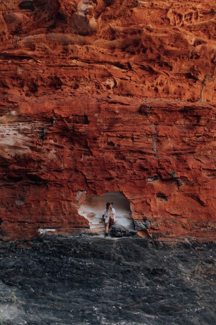 A woman sits beautifully by a striking red cliff, capturing nature's rugged beauty.