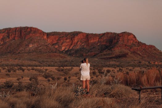 A woman captures the beauty of the desert landscape with red rocky hills at sunset.