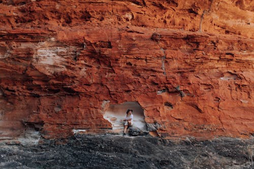 Free Woman Sitting in a Little Cave in a Red Stone Cliff  Stock Photo