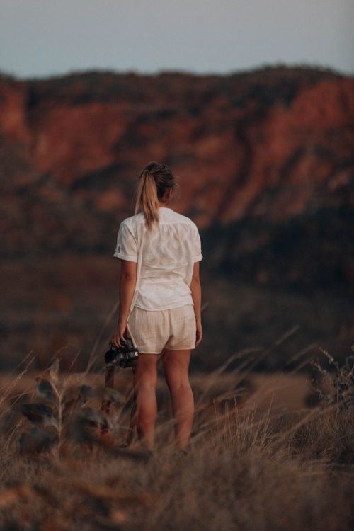 Free Back view of a woman standing in nature holding a camera, showcasing adventure and exploration. Stock Photo
