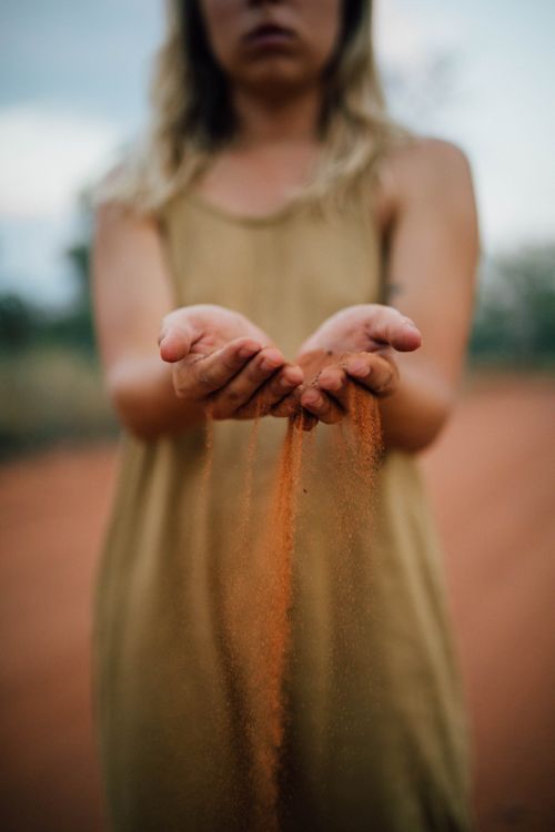 Free A woman gently holding and releasing red sand with a blurred natural background. Stock Photo