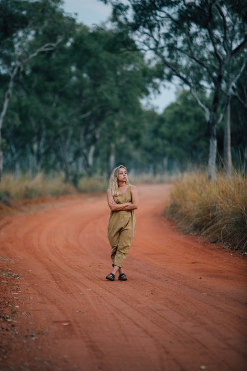 Woman Standing with Arms Crossed in the Middle of an Unpaved Red Sand Road 