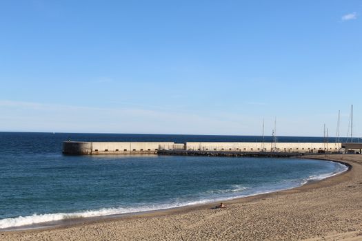 A serene view of a Barcelona beach with a long pier and clear blue sky, capturing the essence of a summer day by the Mediterranean Sea.