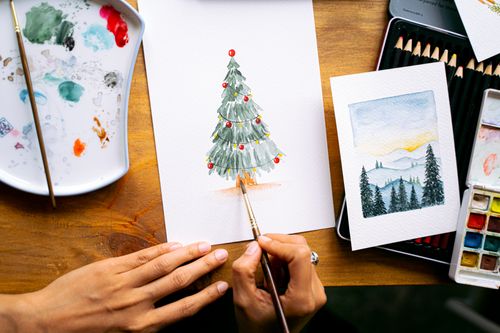 Free Close-up of hands painting a Christmas tree in watercolor, ideal for festive cards. Stock Photo