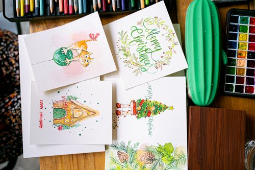 Free Top view of handmade Christmas cards with artistic designs on a wooden table surrounded by art supplies. Stock Photo