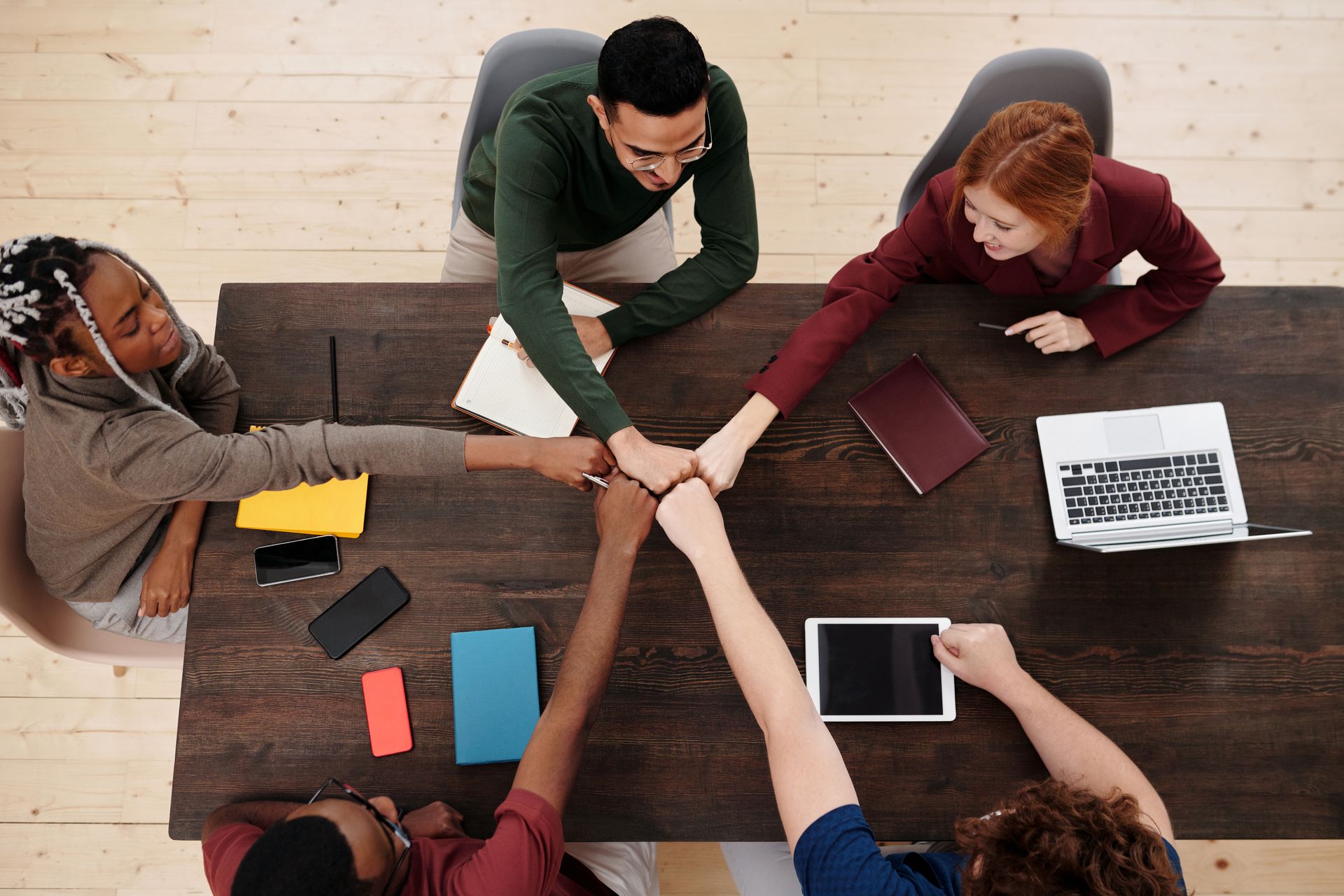 A diverse group of people in a business meeting, showing teamwork with technology on a wooden table.