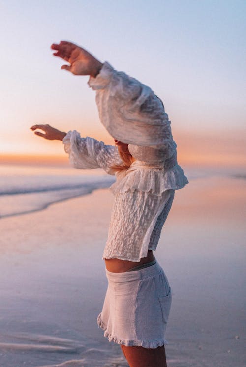 Woman Standing on a Seashore at Sunset with Her Arms Raised 