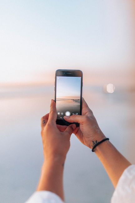 A woman photographs a serene beach sunset using her smartphone.