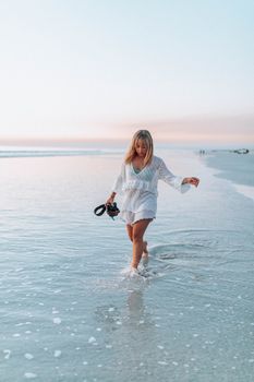 A young woman in white walks along a serene beach at sunset, capturing moments.
