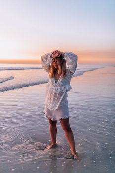 A woman stands peacefully on a beach at sunset, embracing tranquility.