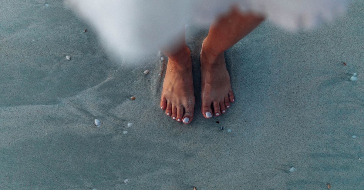 Close-up of woman's feet on sand near the ocean, creating a serene summer vibe.